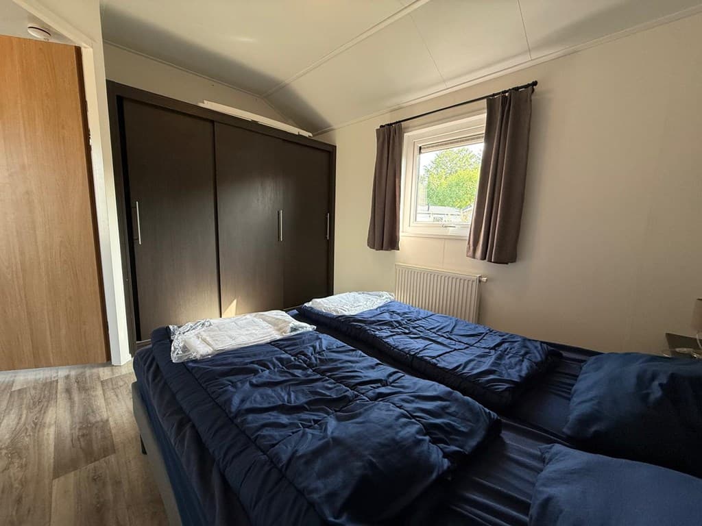 Slaapkamer met twee eenpersoonsbedden, kast en raam met uitzicht op de buitenruimte.