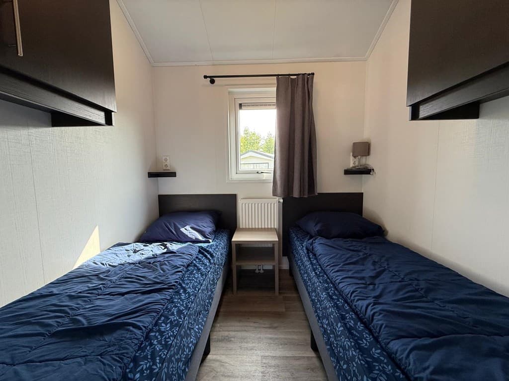 Slaapkamer met twee eenpersoonsbedden, een raam en een nachtkastje tussen de bedden