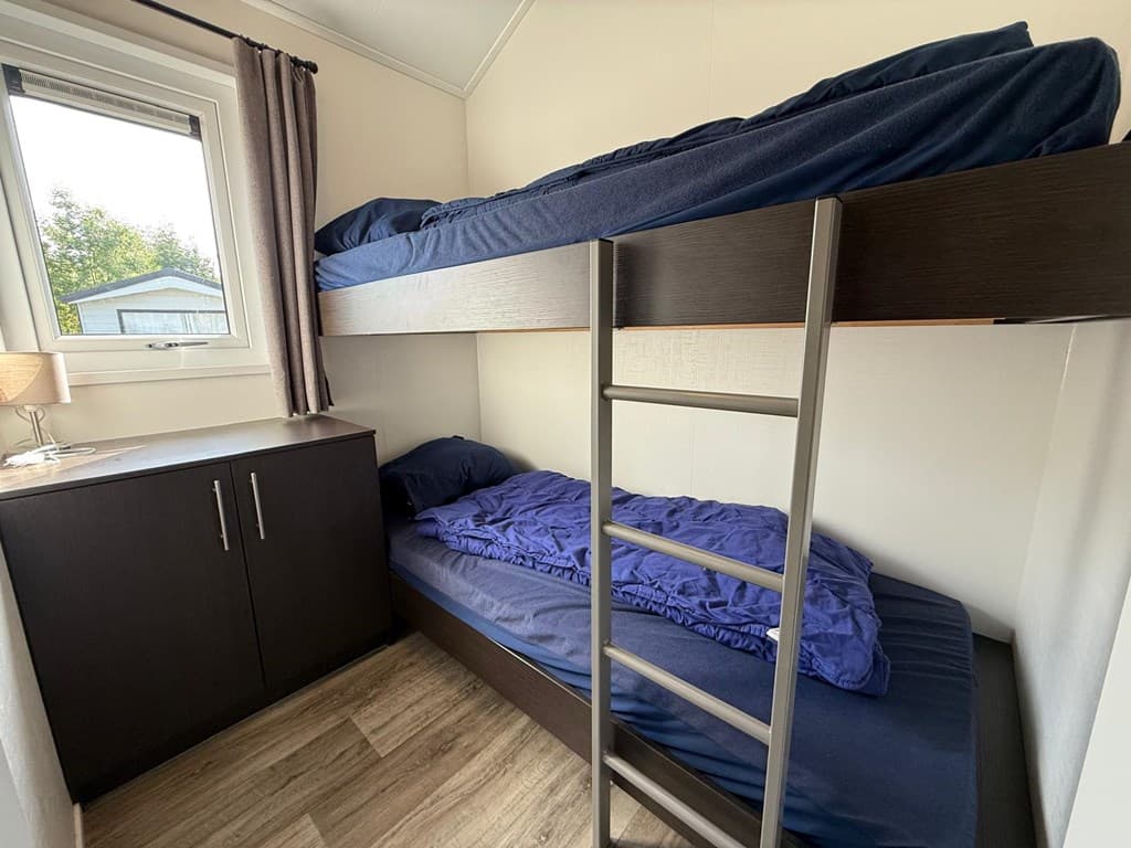 Slaapkamer met stapelbed en een enkele bed, een ladekast en een raam met uitzicht naar buiten