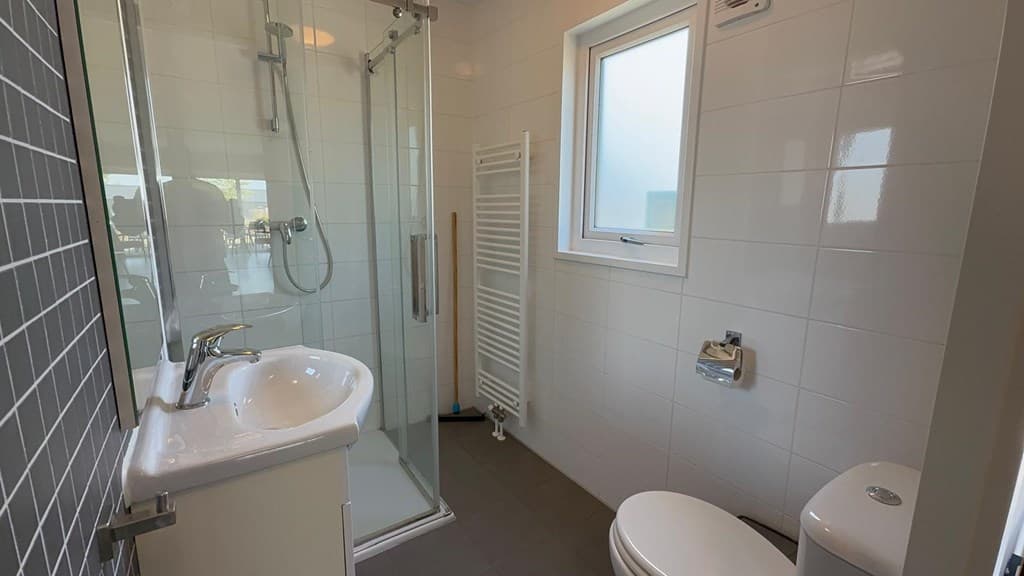 Moderne badkamer met douche, wastafel en toilet, witte tegelwand en raam voor natuurlijk licht