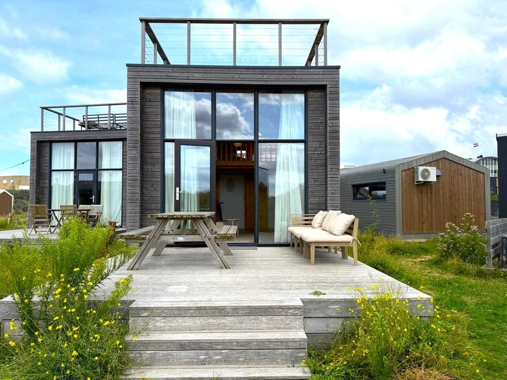Moderne woning met een houten gevel, grote ramen en een dakterras, omringd door gras en bloemen.