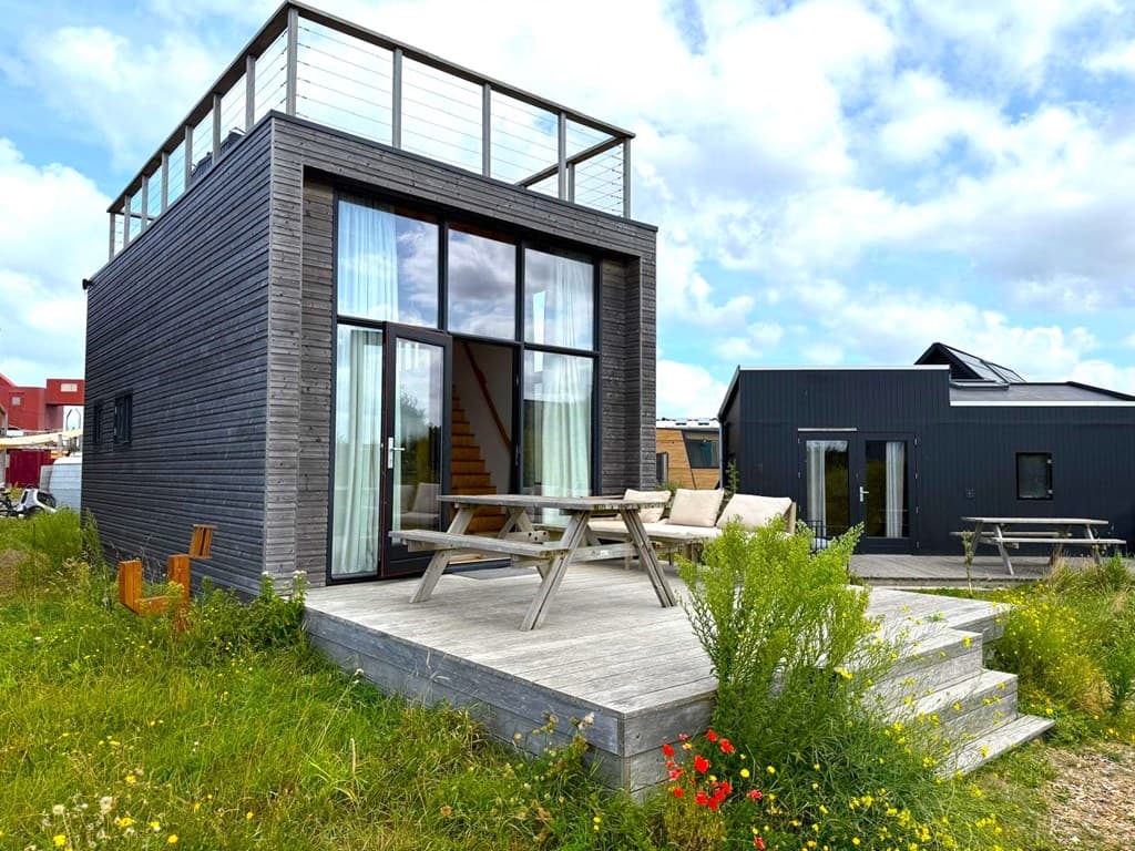 Moderne woning met grote glazen pui, terras met picknicktafel en natuur rondom, gelegen in een open groen veld