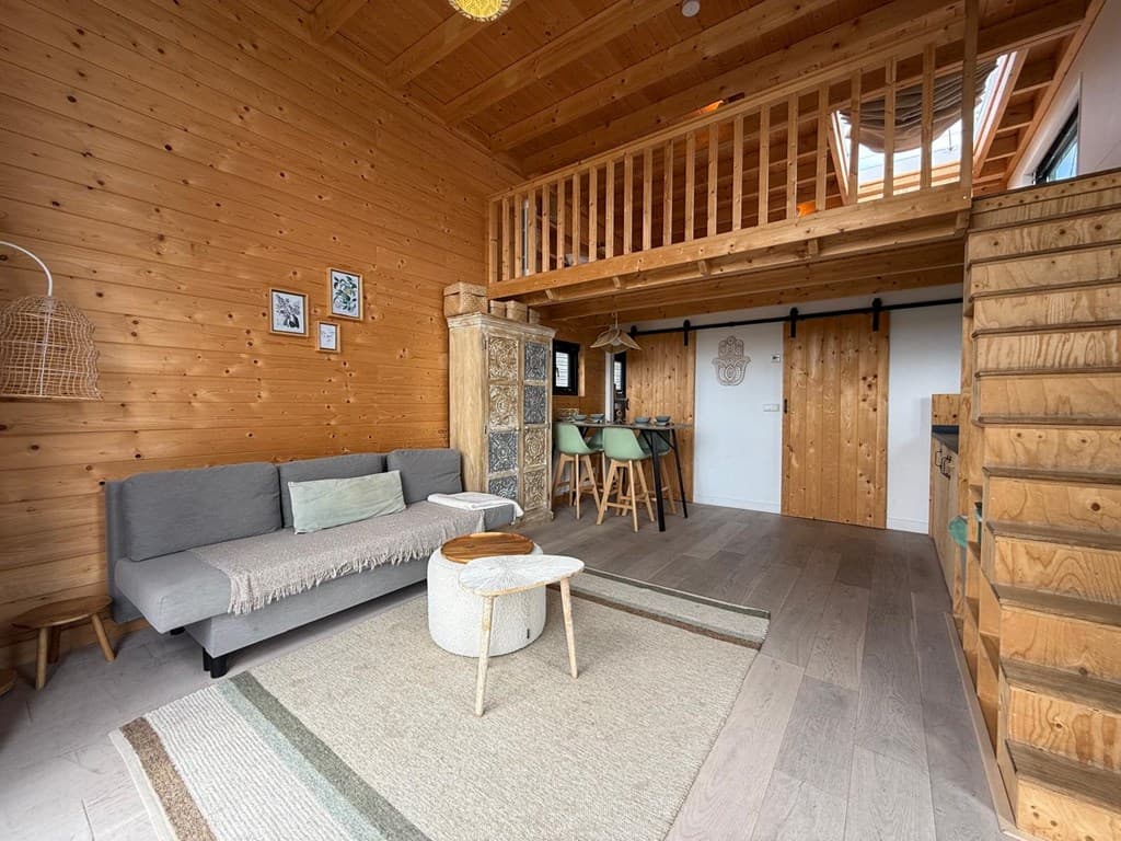 Houten woonkamer met bank, eettafel, trap naar boven en open ruimte met houten plafonds en balken