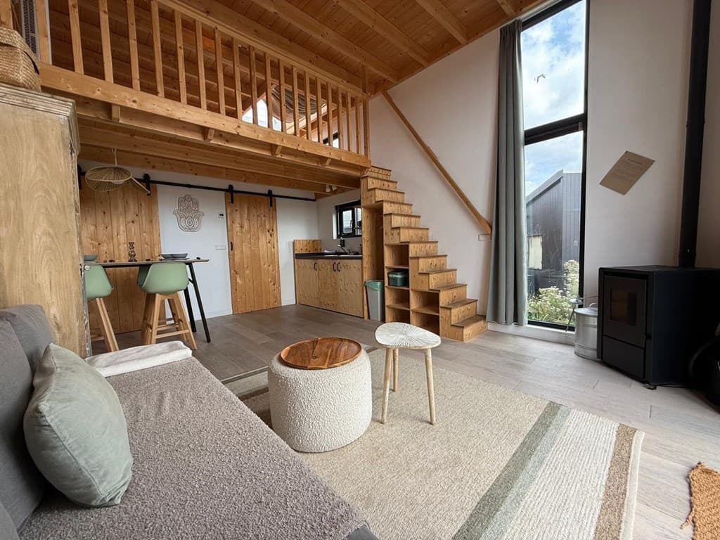 Hedendaagse woonkamer met houten trap naar de bovenverdieping, bank, tafel met stoelen en grote ramen voor natuurlijk licht