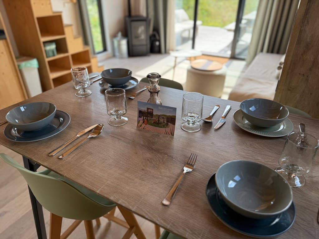 Eettafel met servies en bestek, zicht op de woonkamer met grote ramen en een verwarmingsapparaat op de achtergrond
