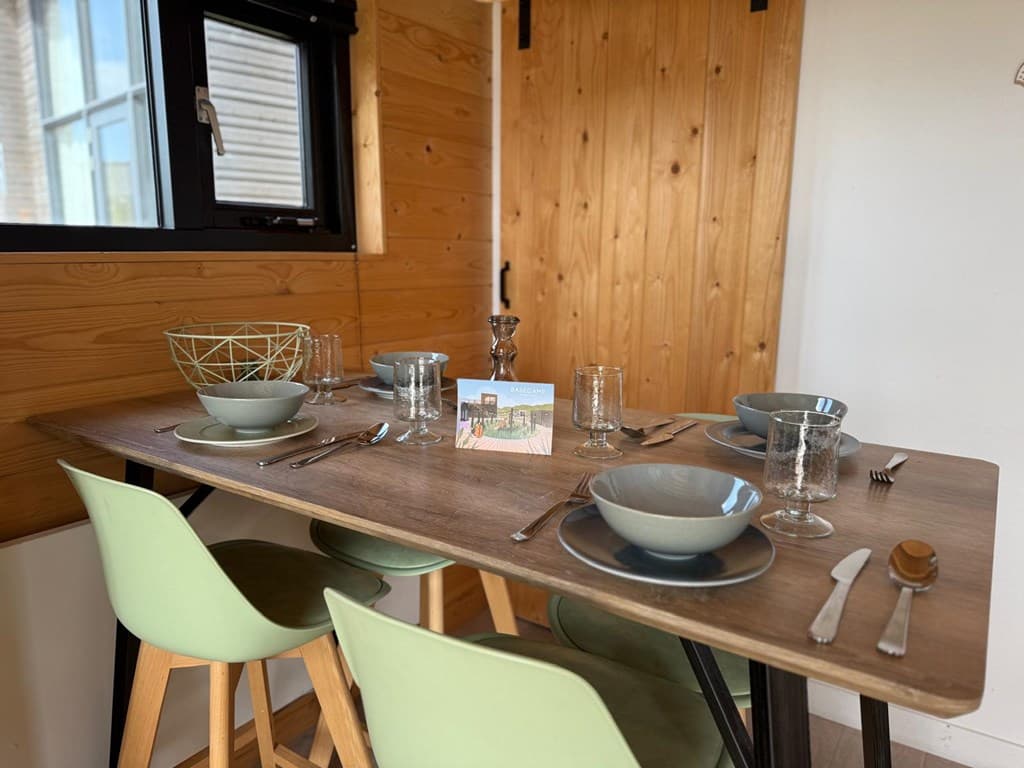Eettafel met borden, glazen en bestek, naast een houten wand en een raam met uitzicht naar buiten