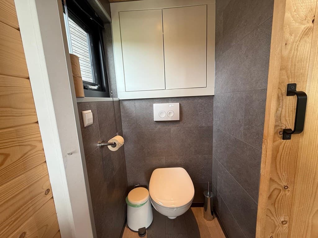 Wit toilet met inbouwkast in een grijze betegelde ruimte met houten accenten en een raam.