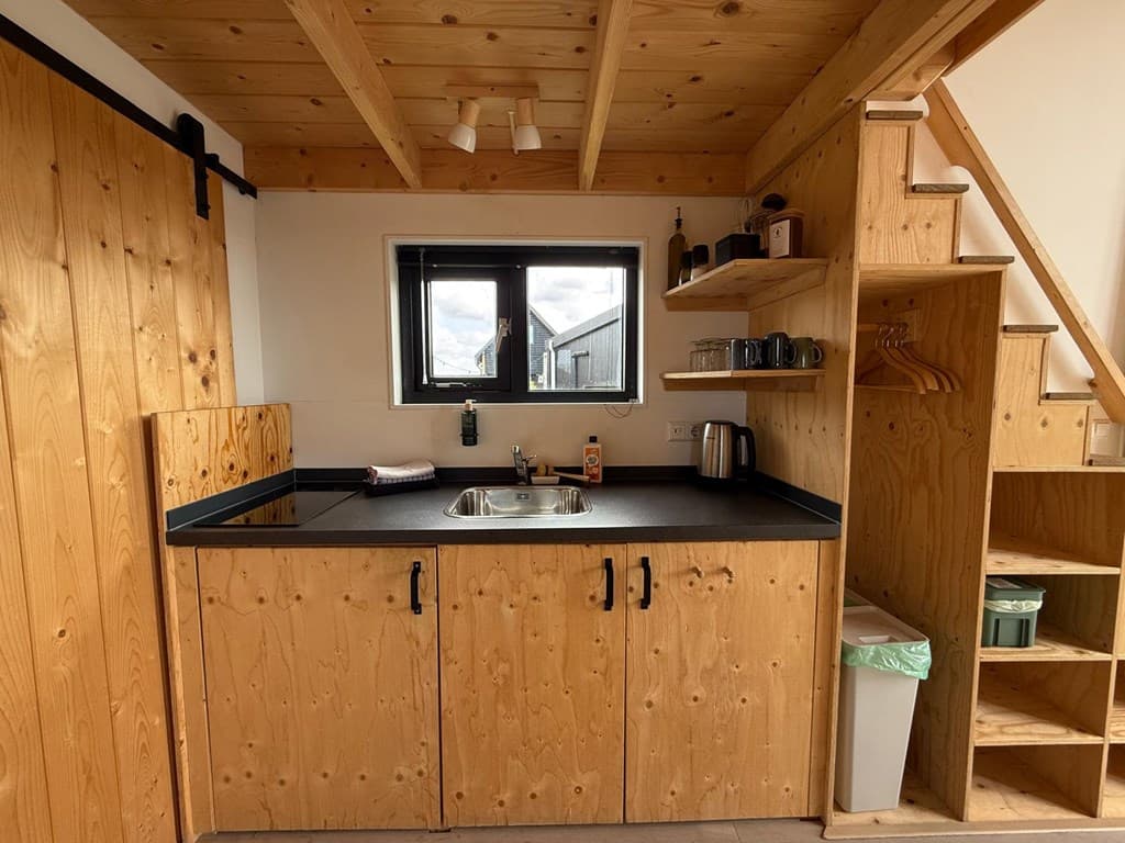 Keuken met houten kasten, spoelbak, en een trap naar een bovenverdieping, met een raam voor natuurlijk licht.