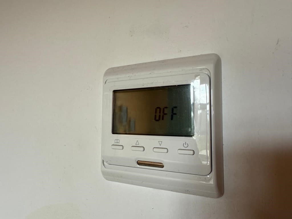 Thermostaat met digitale weergave aan de muur, toont de status 'OFF' en enkele bedieningsknoppen.
