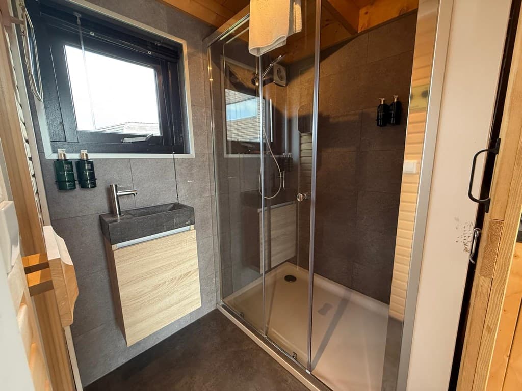 Moderne badkamer met inloopdouche, wastafel met houten kastelement en een raam voor natuurlijk licht.