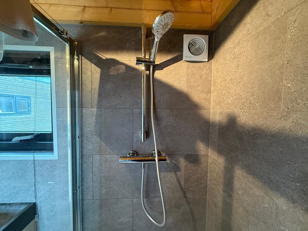 Douche met glanzende handdouche tegen een wand van grijze tegels in een badkamer