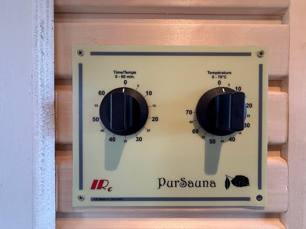 Bedieningspaneel van een sauna met knoppen voor tijd en temperatuur, gemonteerd op een houten wand.