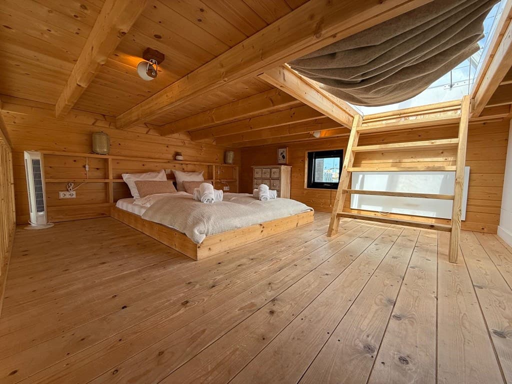 Houten slaapkamer met twee bedden, trap naar bovenverdieping, houten vloeren en grote ramen met uitzicht op de lucht