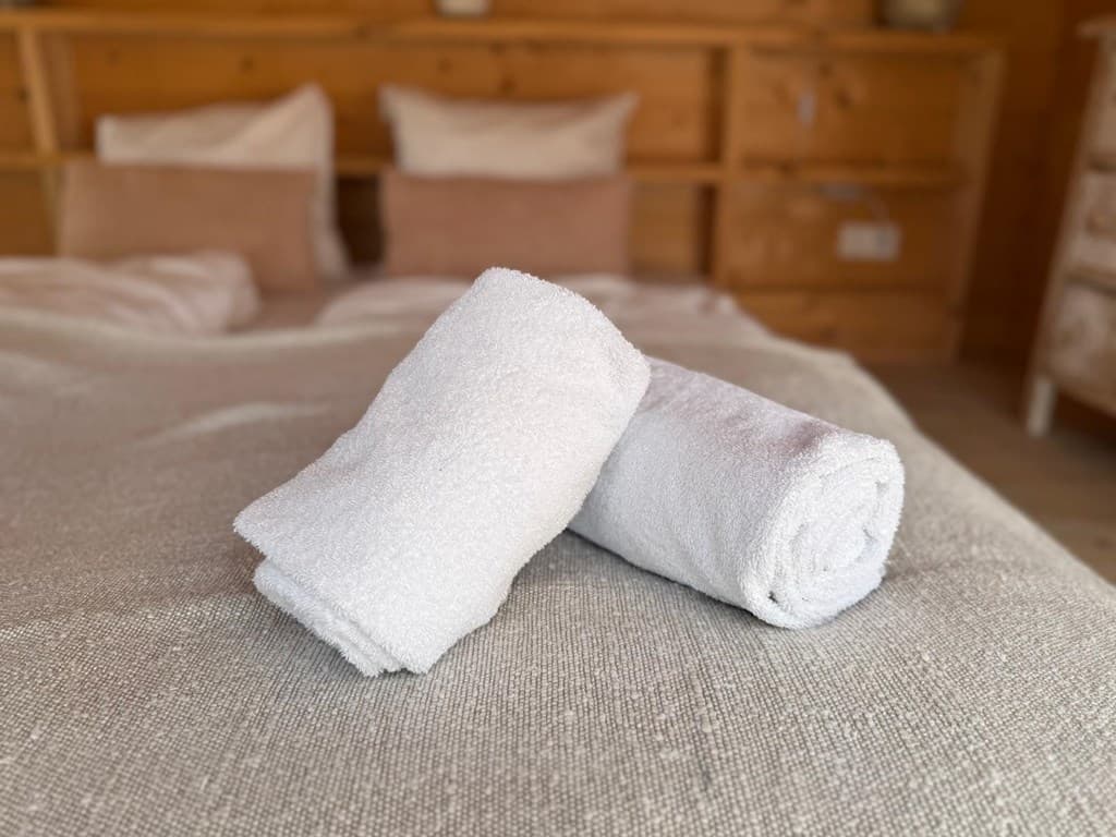 Wit handdoeken liggen op een bed met een lichtgekleurde dekbed en kussens op de achtergrond.