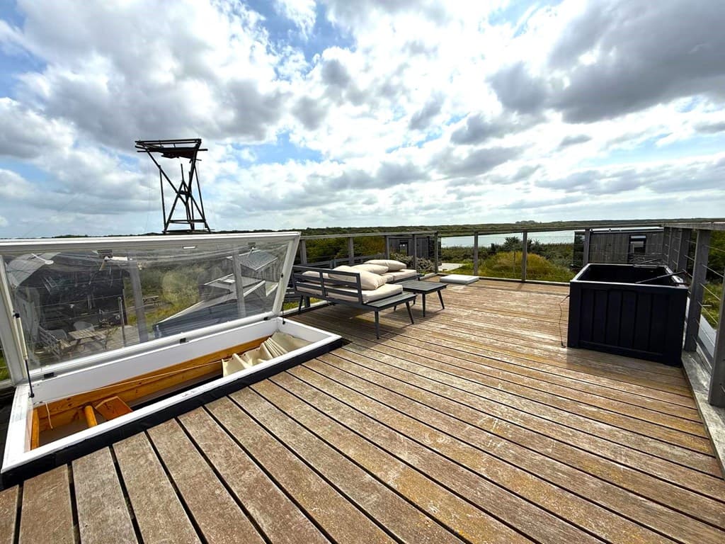 Het dakterras met houten vlonders, ontspanningsmeubilair en een uitzicht op het omringende landschap en de lucht.