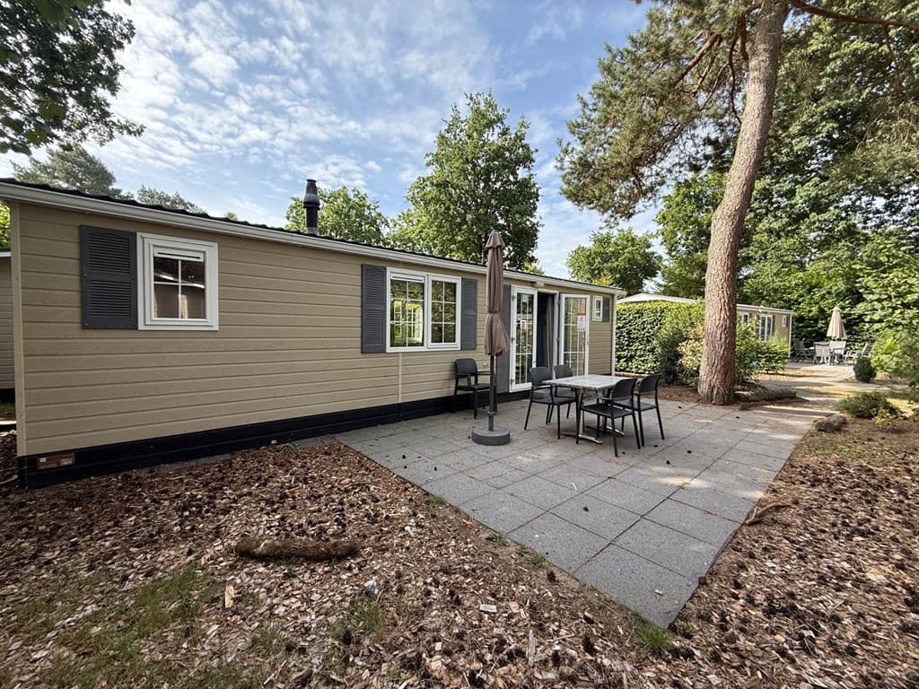 Vrijstaande bungalow met terras, tuinmeubilair en groene omgeving met bomen en andere woningen op EuroParcs De Zanding.