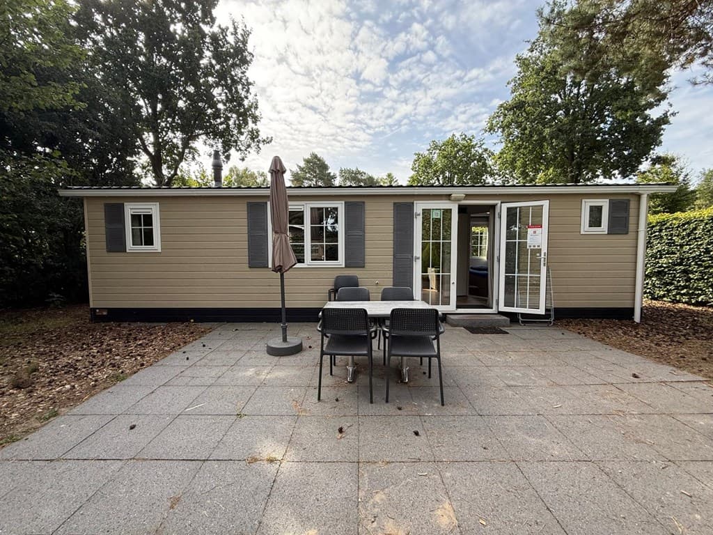 Vakantiewoning met patio, buitenmeubilair en parasol, omgeven door groen en bomen op EuroParcs De Zanding.