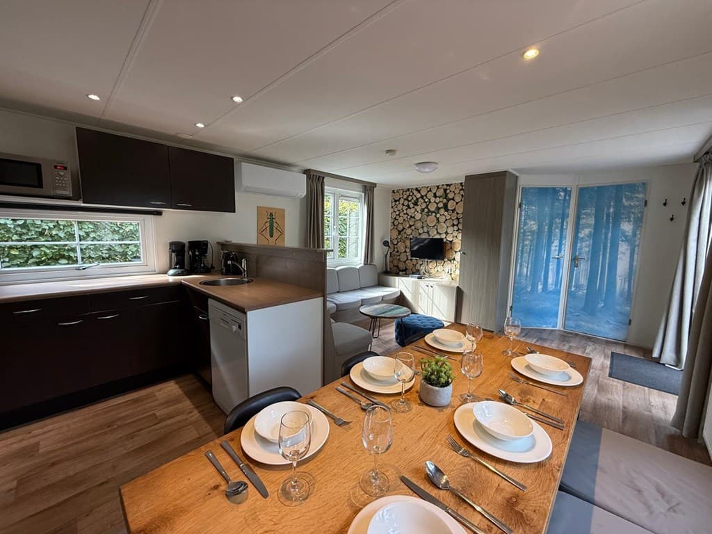 Moderne woning met open keuken, eettafel, zithoek en toegang tot een terras met uitzicht op een boswand.