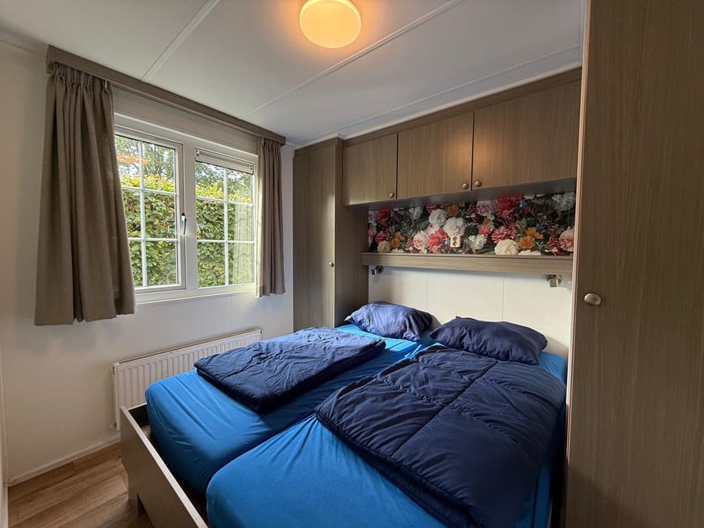 Slaapkamer met twee losse bedden, een raam met zicht op groen en een kast met bloemenmotief boven de bedden