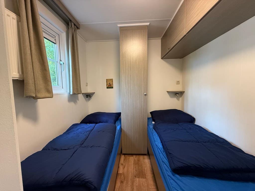 Twee aparte bedden met blauwe dekbedden in een eenvoudige slaapkamer met houten vloer en kast.