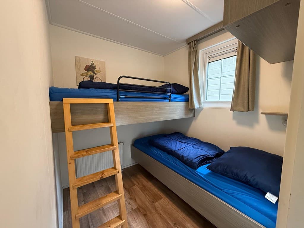 Slaapkamer met stapelbed en eenpersoonsbed, houten ladder en raam met uitzicht op buiten.