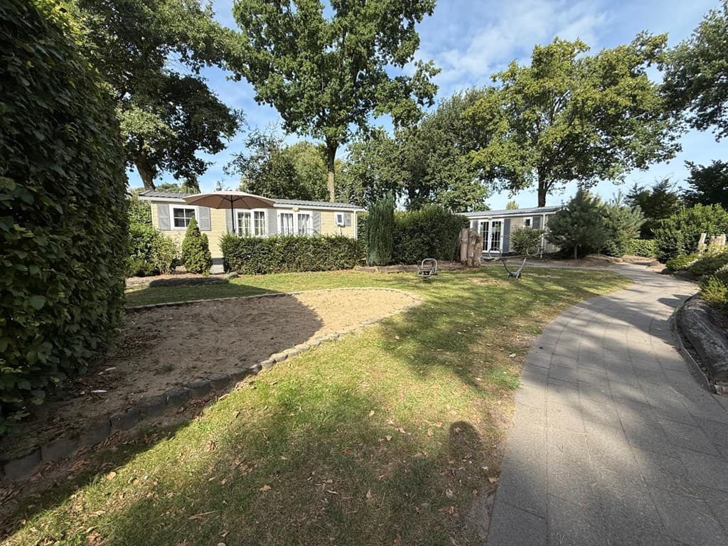 Groen terrein met zandbak en paden langs vakantiewoningen omgeven door bomen en struiken