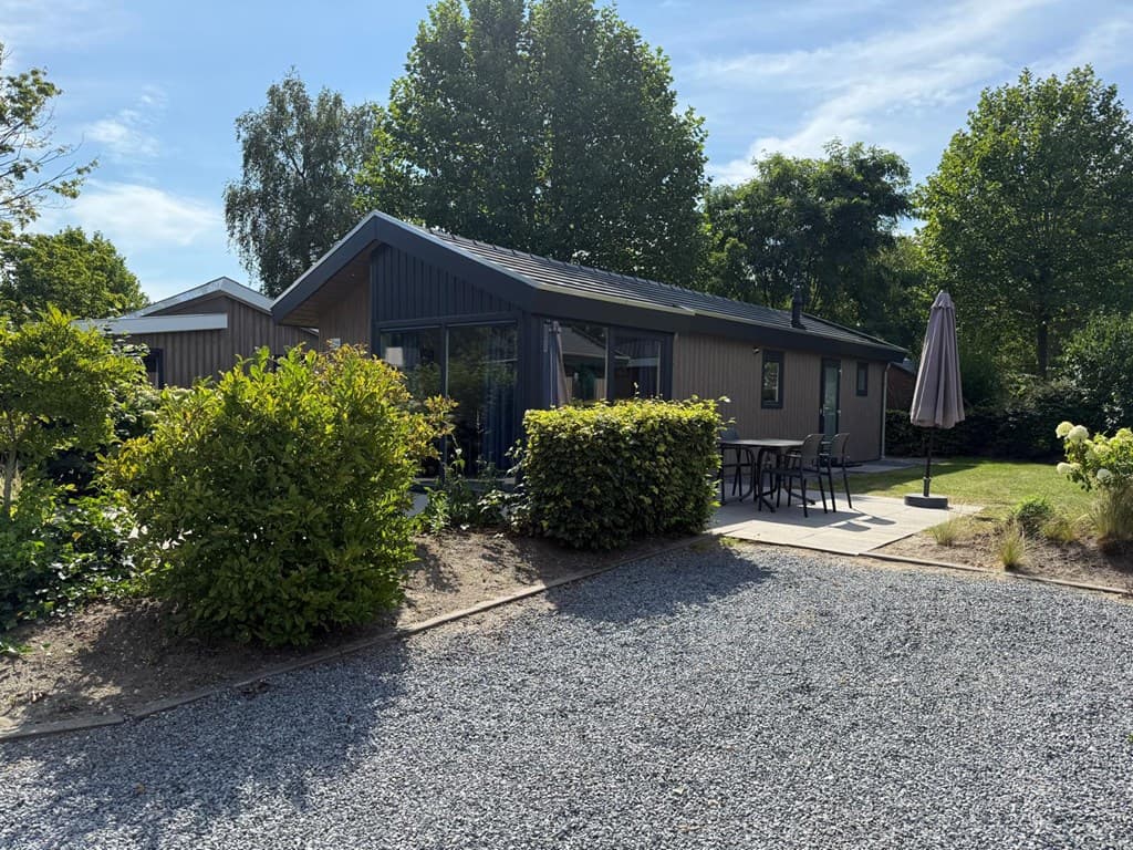 Moderne vakantiewoning met een terras en parasol, omgeven door groen en grind.