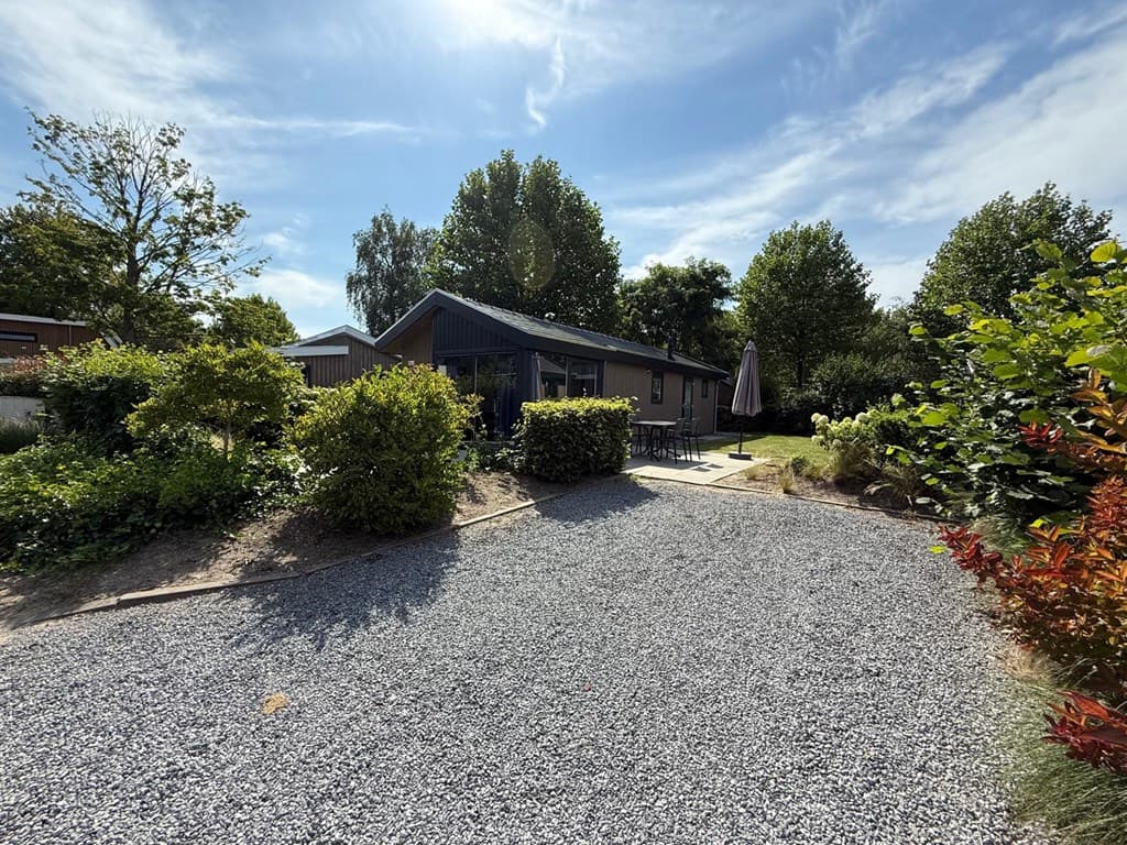 Vakantiehuis met tuin en terras, omringd door groene bomen en struiken, grindpad naar de ingang toegevoegd.