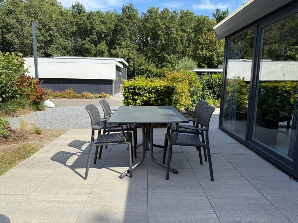 Terras met een tafel en vier stoelen, omringd door groen en uitzicht op andere vakantiehuisjes
