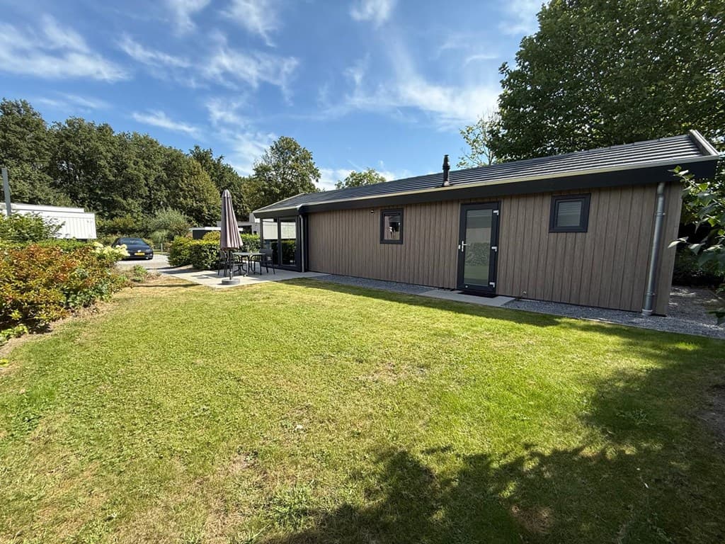 Moderne vakantiewoning met een groene tuin, terras en parasol in EuroParcs Zuiderzee, omringd door bomen.