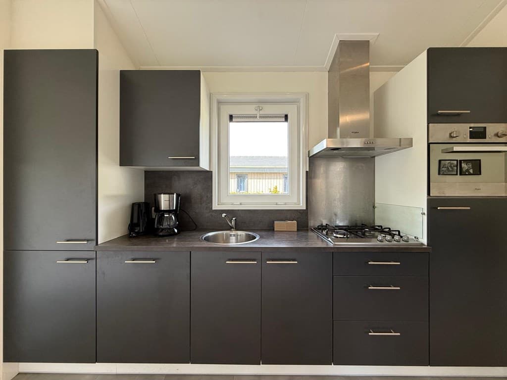 Keuken met moderne kastdeuren, een spoelbak, gasfornuis en een oven, met een raam dat uitzicht geeft op de buitenruimte.
