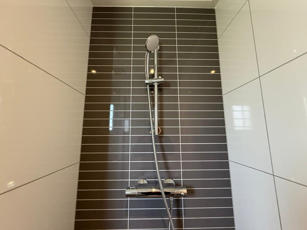 Douche met een moderne handdouche en betegeling in lichte en donkere kleuren