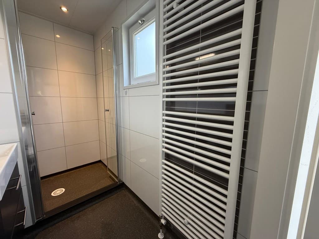 Moderne badkamer met inloopdouche, handdoekradiator en tegelwanden in lichte kleuren.