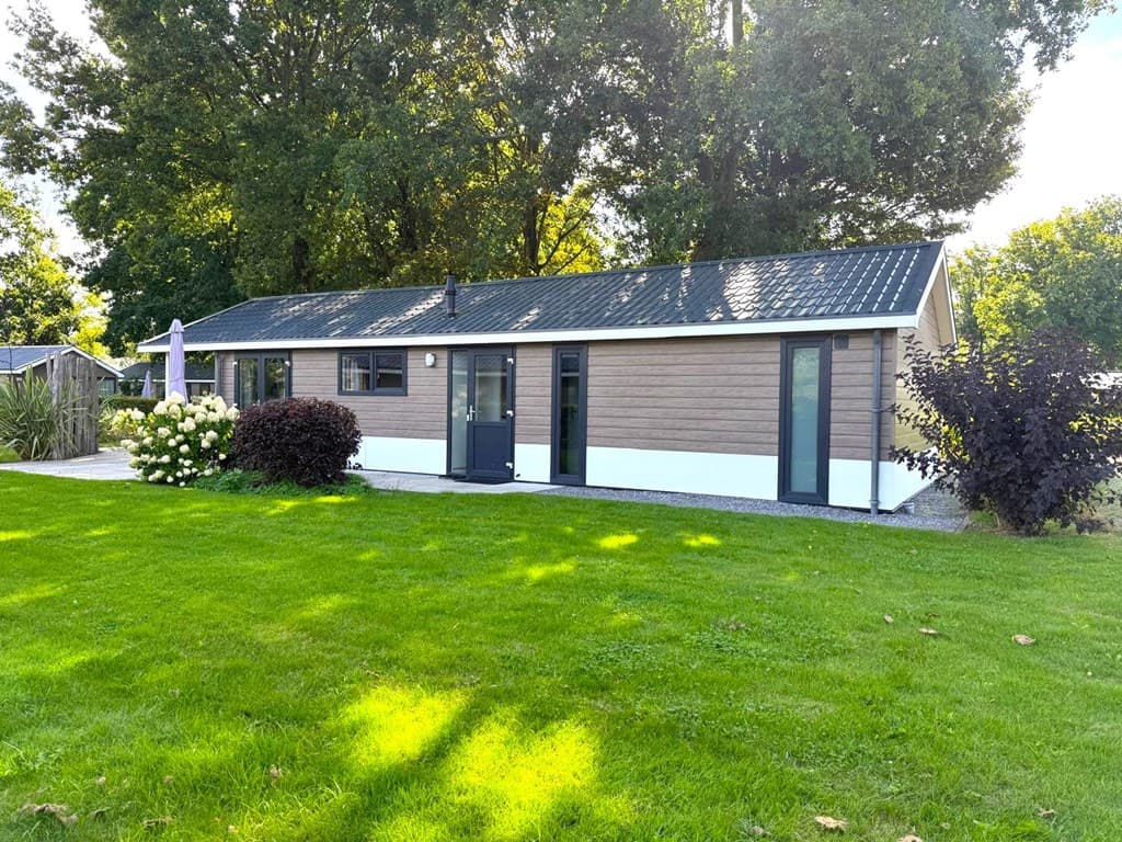Twee vrijstaande woningen omringd door groen gras en bomen met een moderne uitstraling en grote raampartijen.
