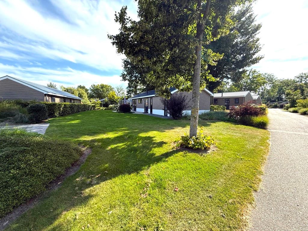 Moderne vakantiewoning met groene tuin en bomen, gelegen in EuroParcs Zuiderzee, omringd door gras en paden.