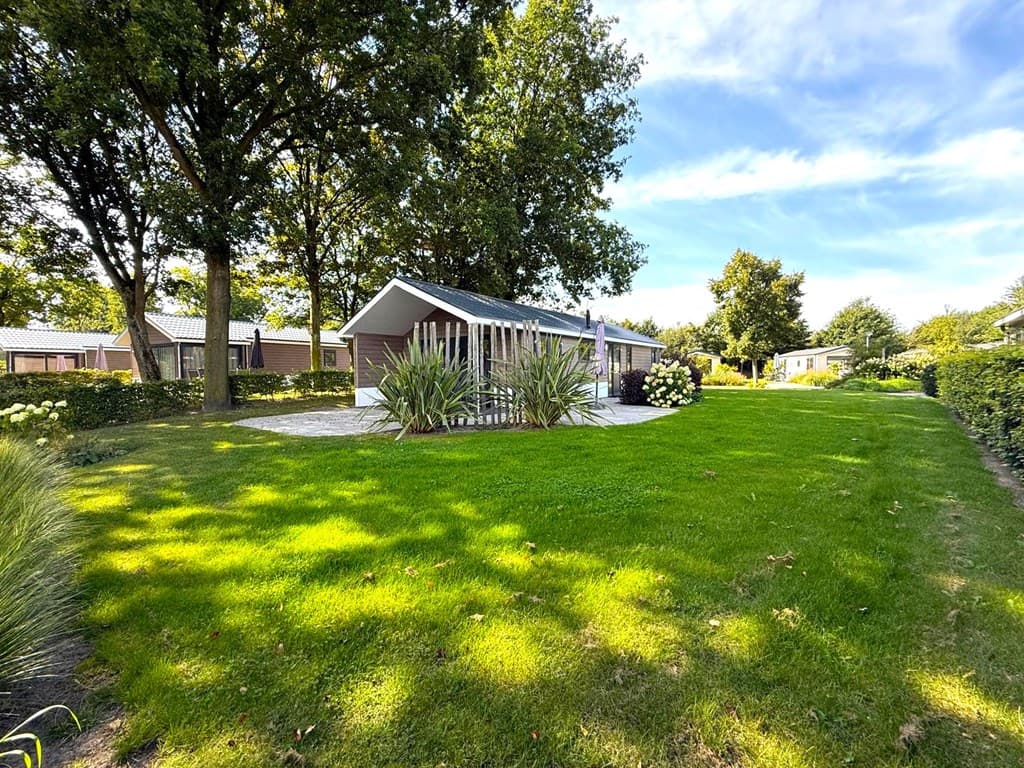 Moderne vakantiewoning omringd door groen gras en bomen, met een terras en tuin op EuroParcs Zuiderzee.