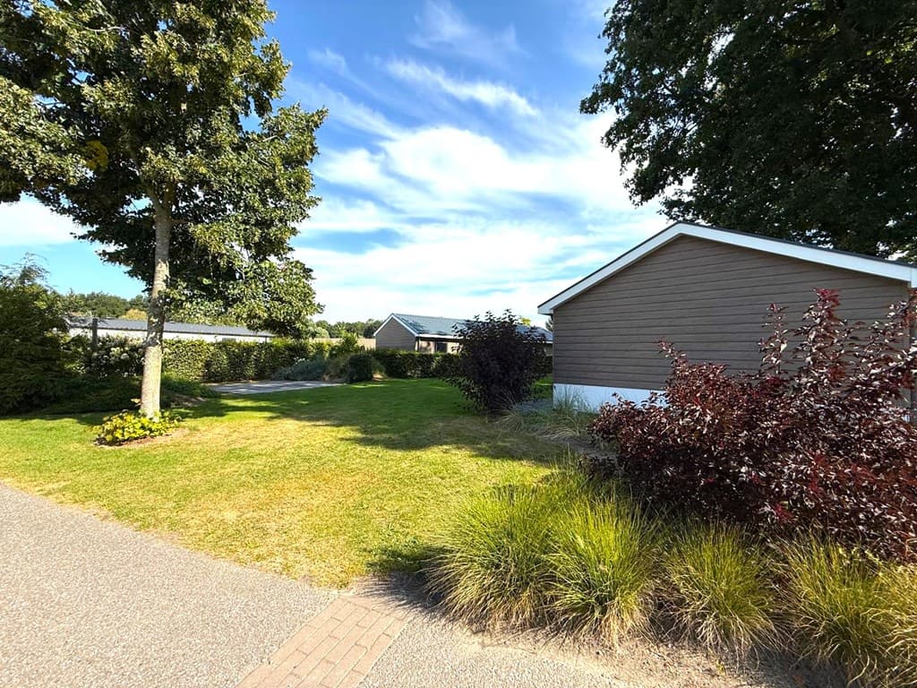 Woningen en groene tuinen met bomen en struiken in EuroParcs Zuiderzee, Biddinghuizen onder een blauwe lucht.