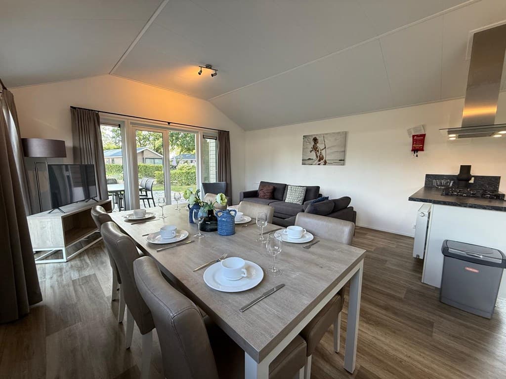 Woonkamer met eettafel, bank en moderne keuken in een vakantiewoning met uitzicht op buitenveranda.