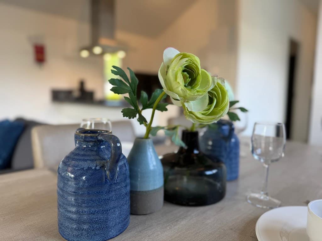 Verschillende vazen met bloemen op een houten tafel in een gezellig interieur met moderne keuken op de achtergrond