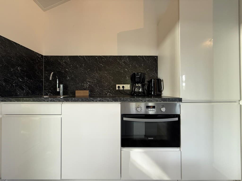 Moderne keuken met witte kasten, zwarte marmeren werkblad, oven en koffiezetapparaat.