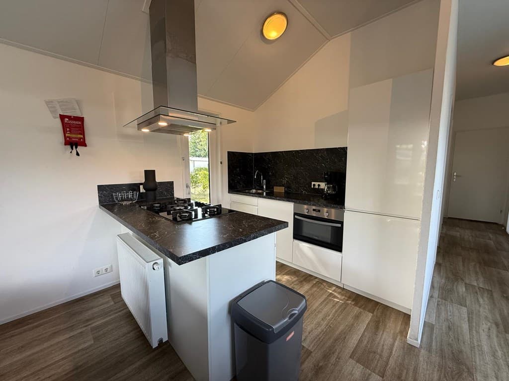 Moderne open keuken met zwarte werkbladen, een gasfornuis en inbouwapparatuur, lichte houten vloeren en een radiateur.