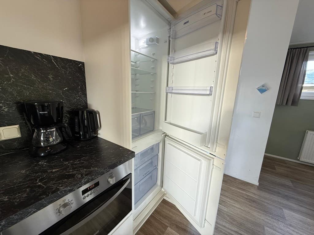 Interieur van een keuken met een open koelkast, koffiezetapparaat en oven op een zwart aanrecht.