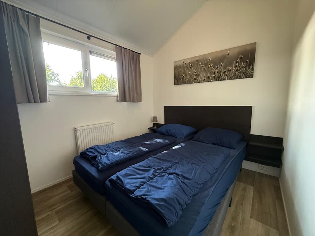 Slaapkamer met twee eenpersoonsbedden, raam met gordijnen en een groot schilderij aan de muur.
