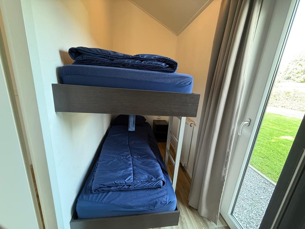 Slaapkamer met stapelbed, blauwe matrassen en zicht op de tuin door de glazen deur.