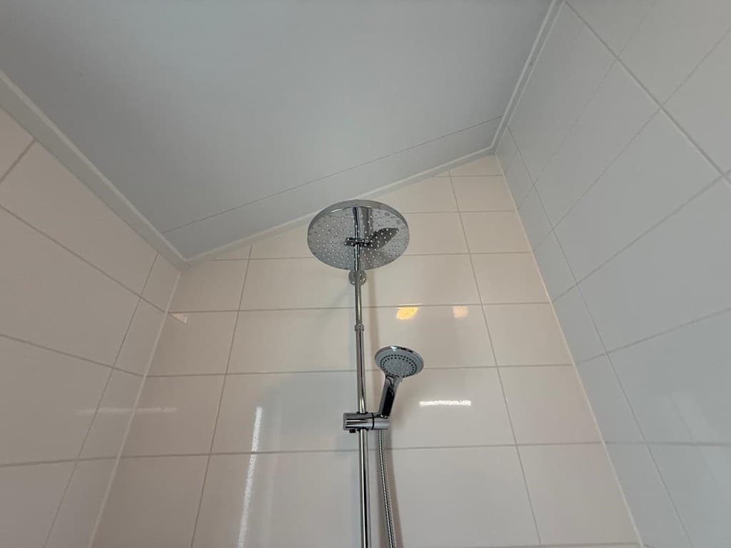 Douchekop en -wand in een badkamer met witte tegels en een licht plafond