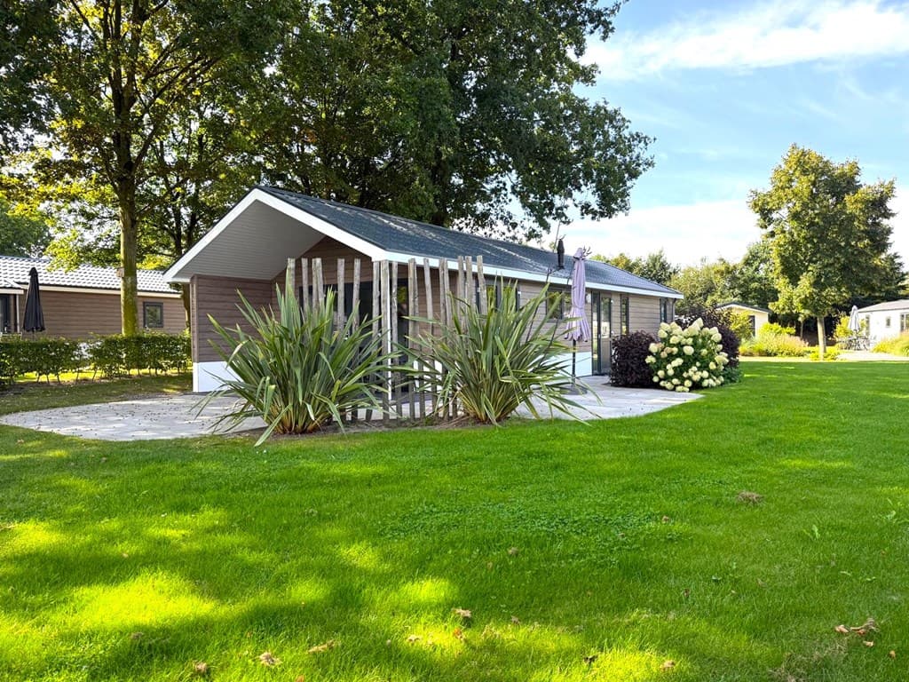 Vakantiewoning met een groene tuin, moderne gevel en houten elementen, omgeven door bomen en struiken.