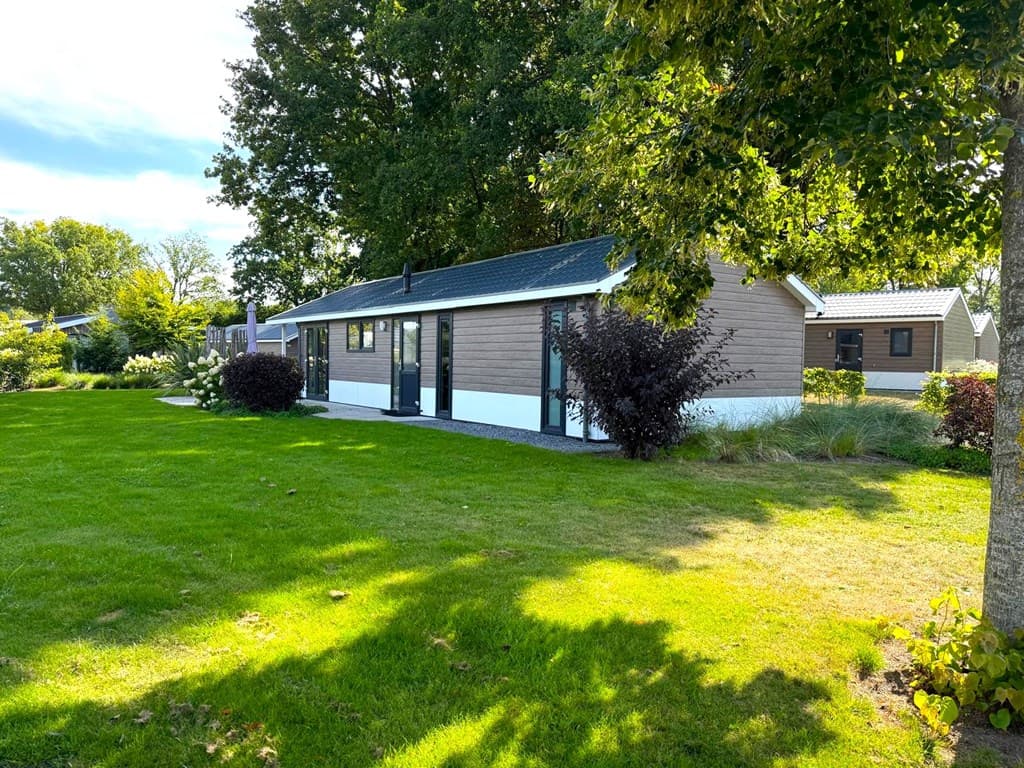 Uitzicht op een vrijstaande vakantiewoning met een groene tuin en planten rondom, gelegen op EuroParcs Zuiderzee.