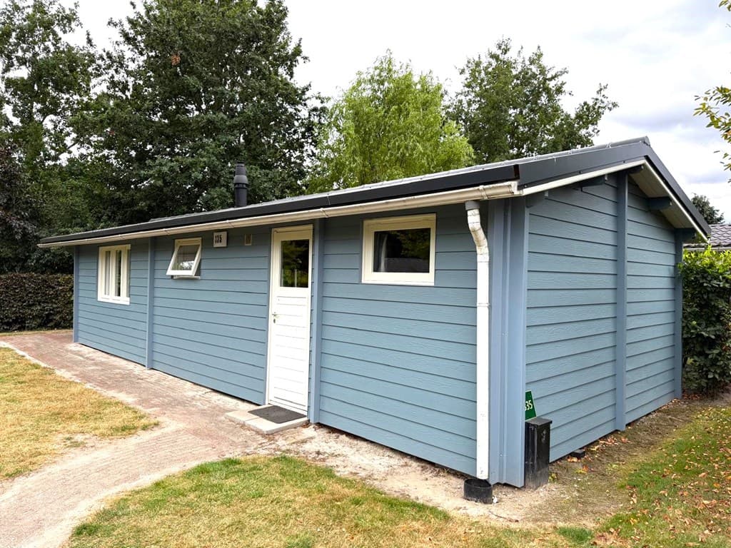 Moderne bungalow met blauwgrijze gevel, groene tuin en pad naar de ingang met ramen aan de zijkant.