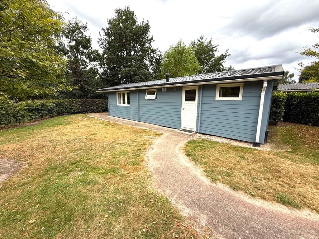 Moderne vakantiewoning met blauwe gevel, omgeven door gras en bomen, met een pad naar de ingang.