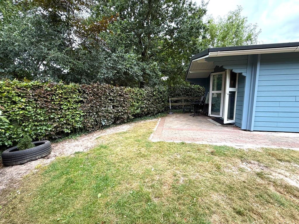 Buitenzicht op een woning met een betegeld terras, grasveld en groene heggen rondom de tuin